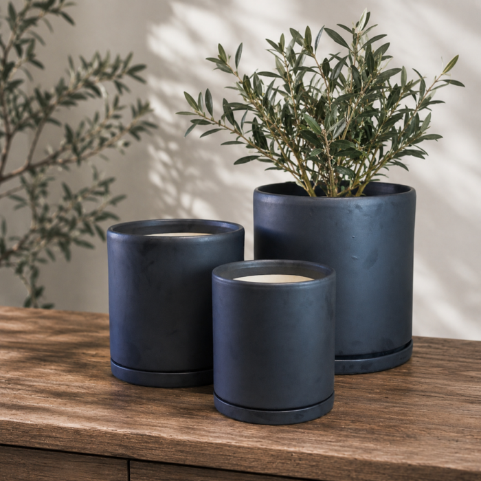 Three matte black cylinder pots with water trays and plants